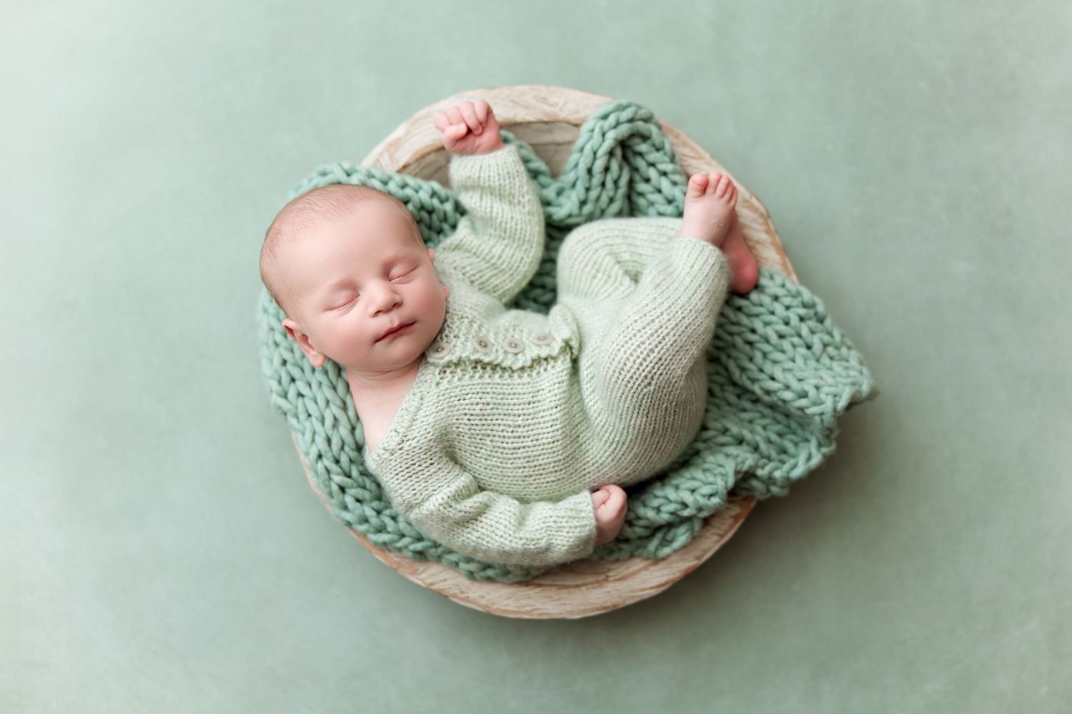 Newborn baby boy wrapped in soft mint green and white knitted blankets lying in decorative bowls for Monterey newborn studio session.