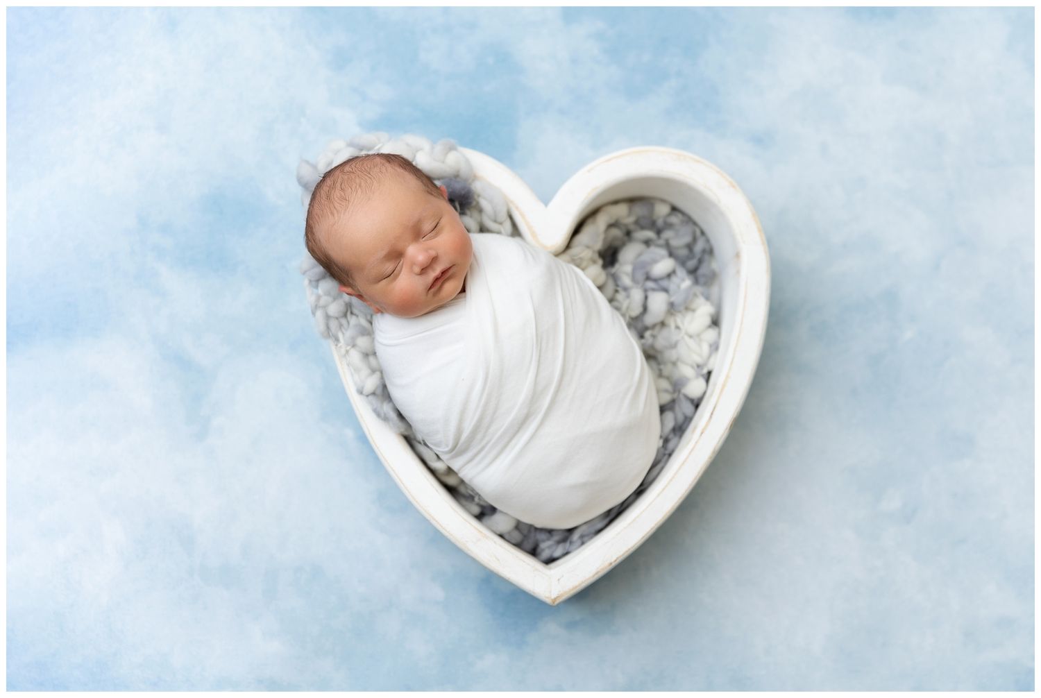 A series of black and white newborn photography images showing a baby sleeping in heart-shaped bowls and props.