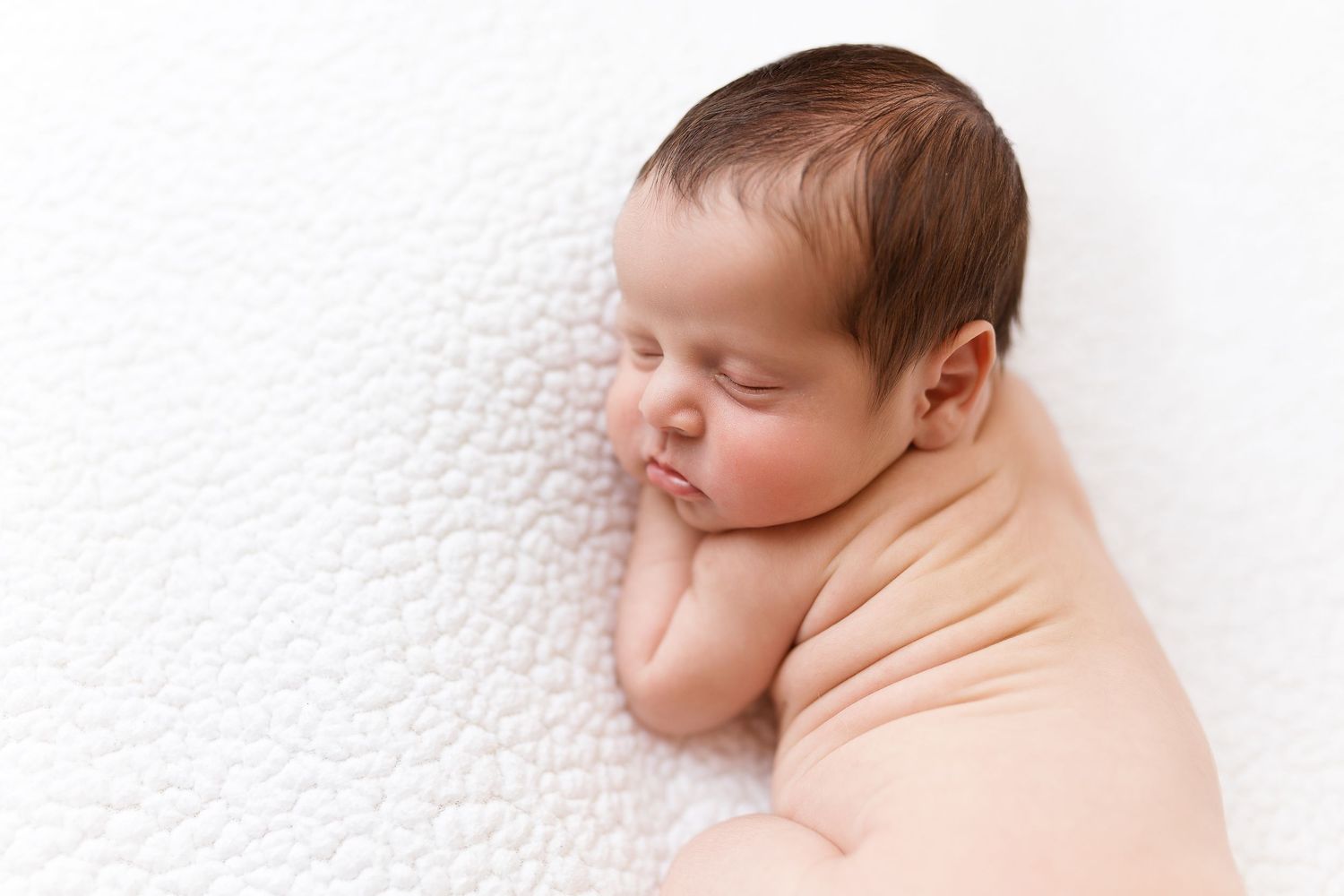Serene newborn baby wrapped in peach fabric against white textured background.