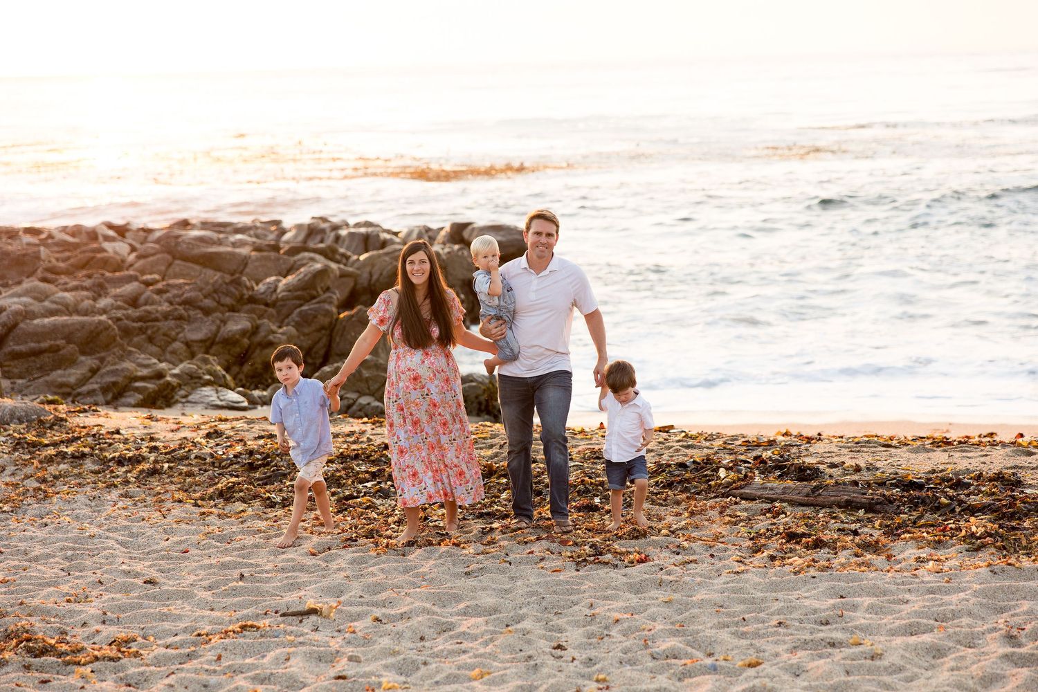 Family with children walks together along rocky beach shore at sunset.