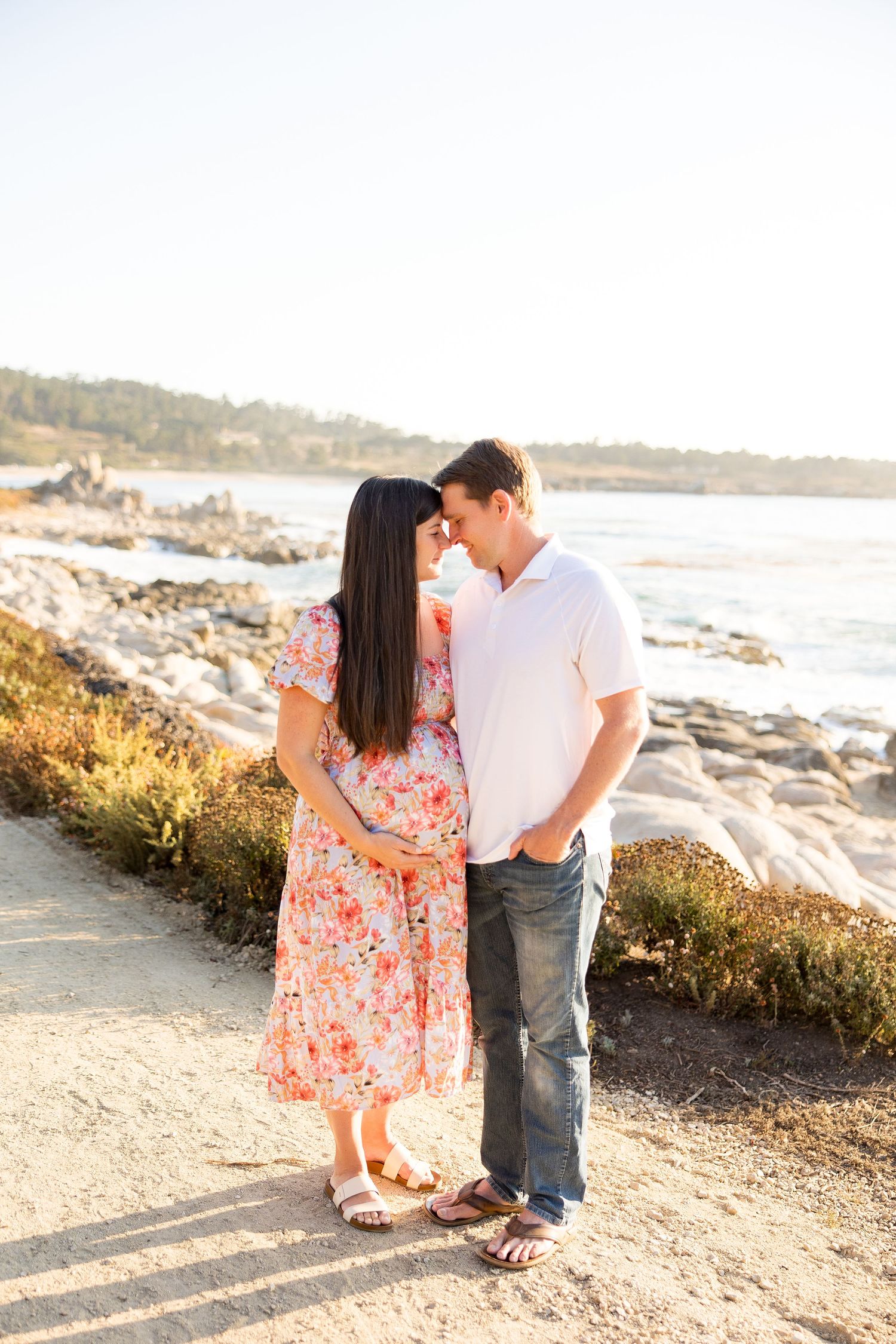 A couple shares a romantic moment at sunset on a rocky coastal beach.