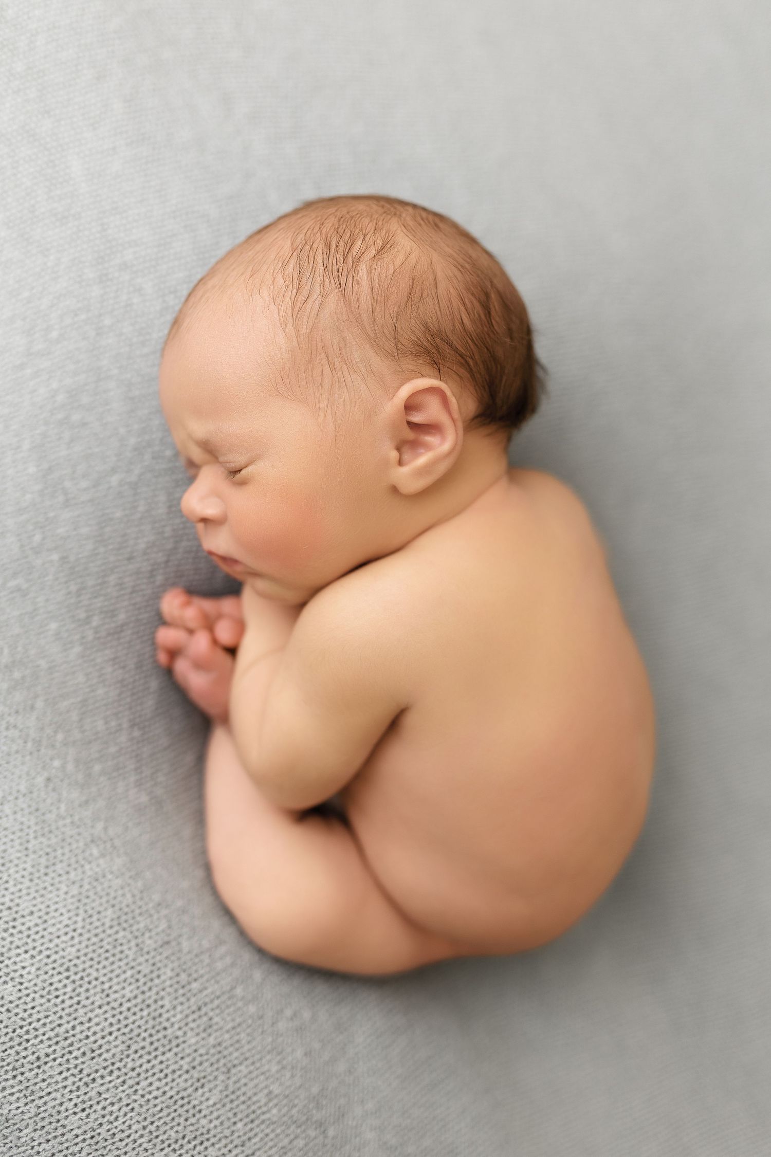 Sleeping newborn baby curled up in fetal position on soft gray fabric background.