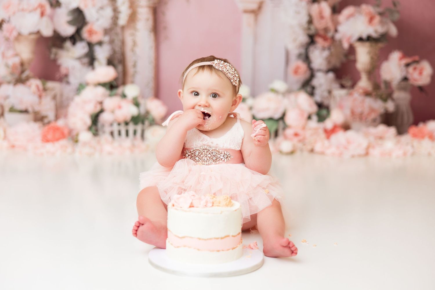 Baby's first birthday cake smash session with pink roses and white architectural backdrop.
