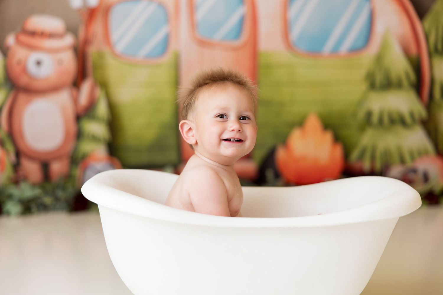 Clean white bathtub prop against whimsical camping-themed backdrop for baby photography.