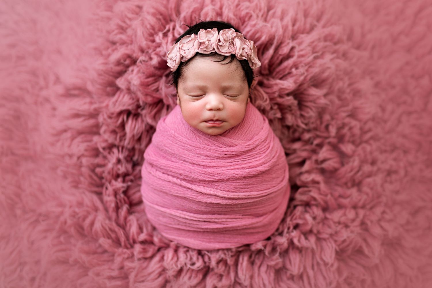 Newborn photography session with pink textured backdrop and wrapping.