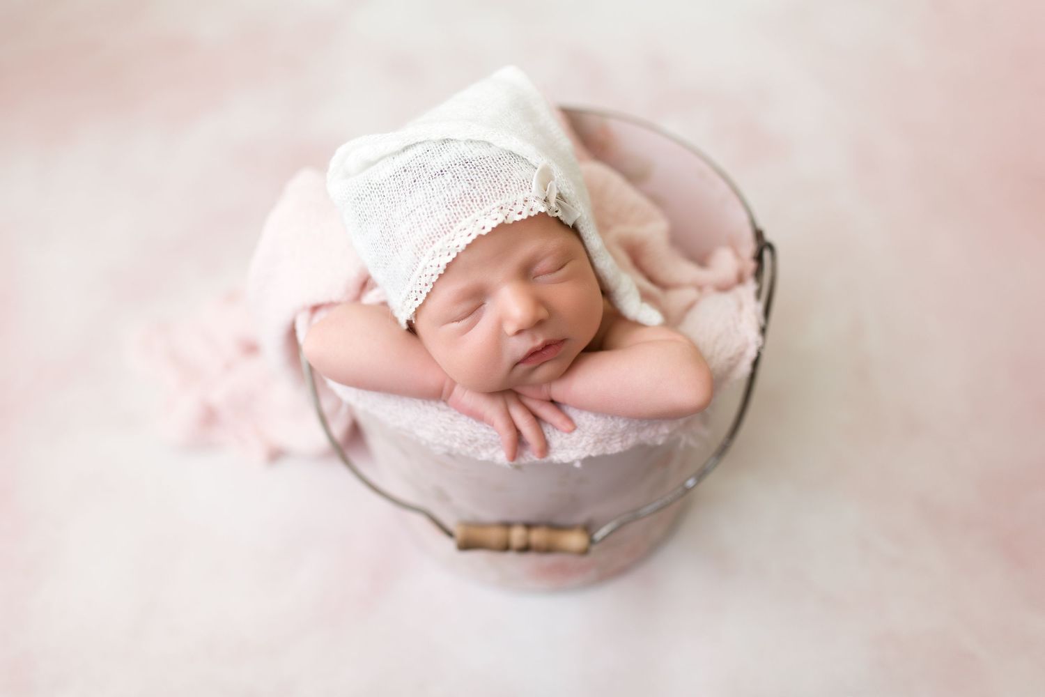 Sleeping newborn in white bonnet nestled in pink round basket.