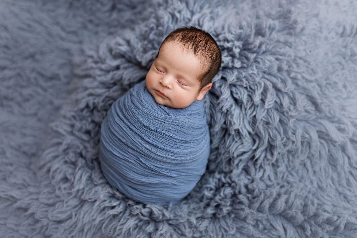 Sleeping newborn wrapped in soft gray fabric on matching textured background.