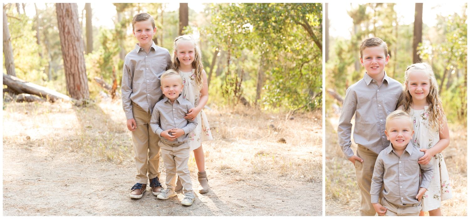 A family in coordinated grey outfits poses together in a wooded outdoor setting during a photo session.