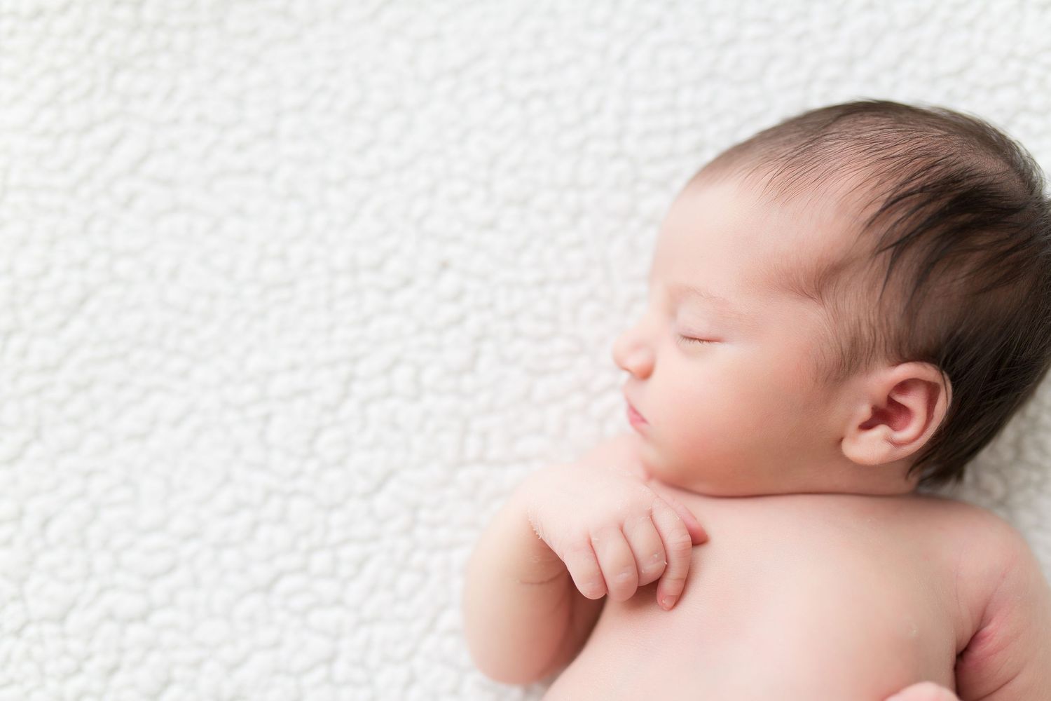 Sleeping newborn baby with soft features resting peacefully against white textured background.