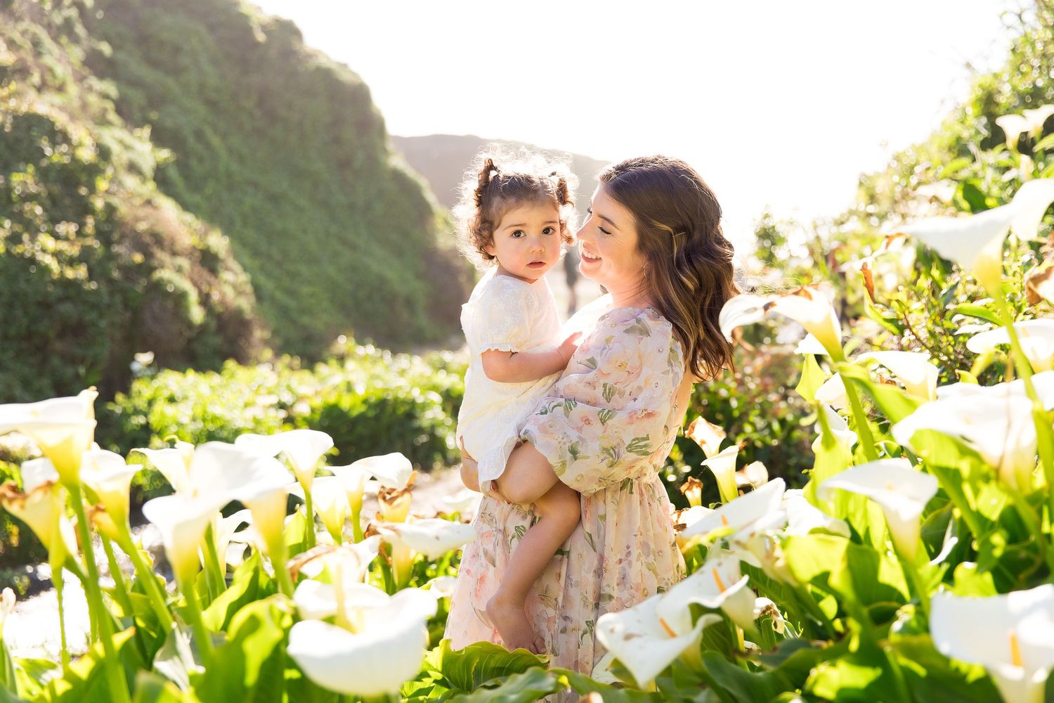 Family moment captured among blooming white calla lilies on a coastal hillside.