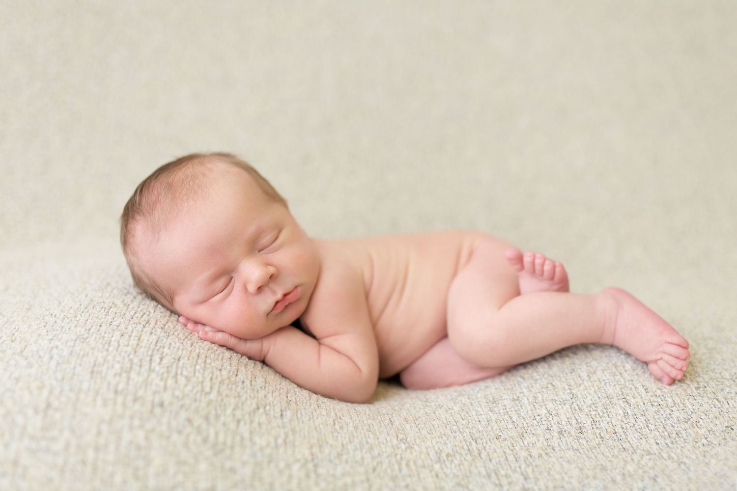 Side view of sleeping newborn on beige textured backdrop.