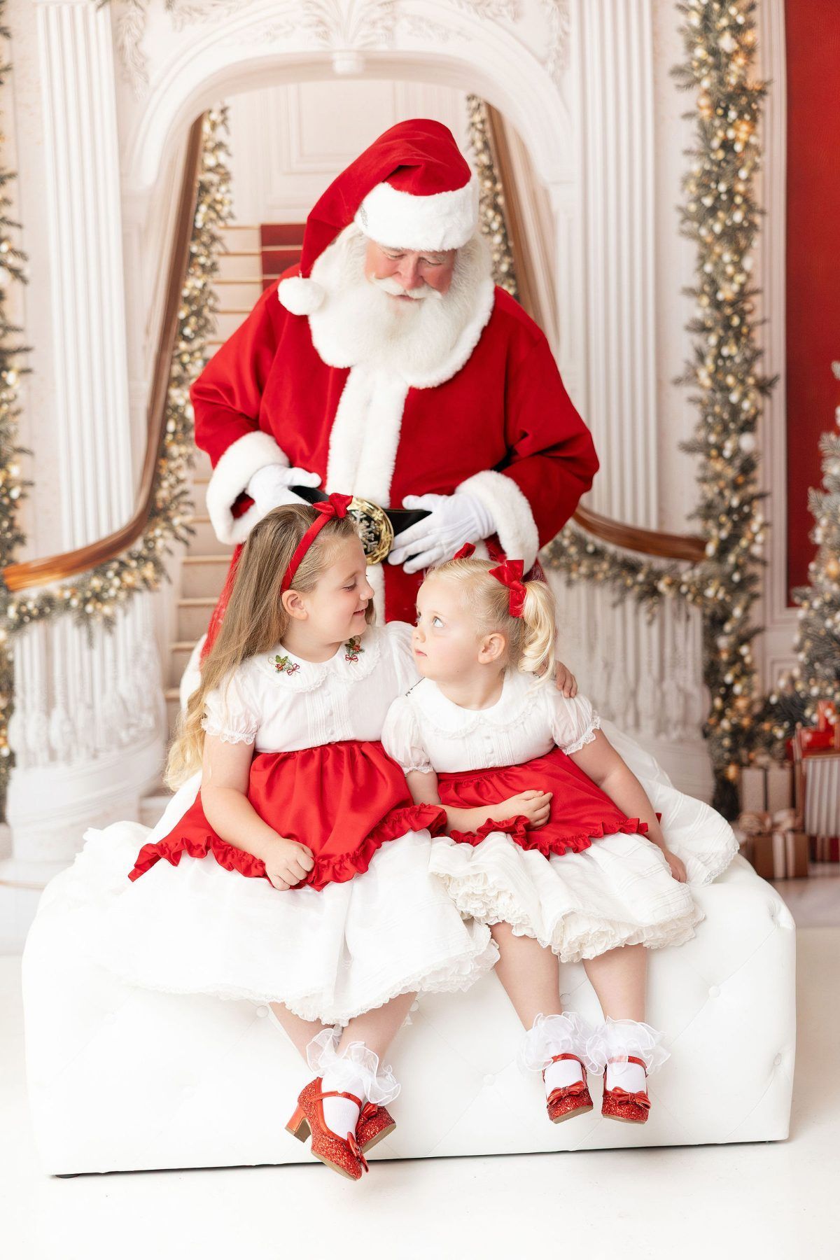 Sisters in red Christmas dresses whispering Christmas wishes to Santa at a Pacific Grove studio