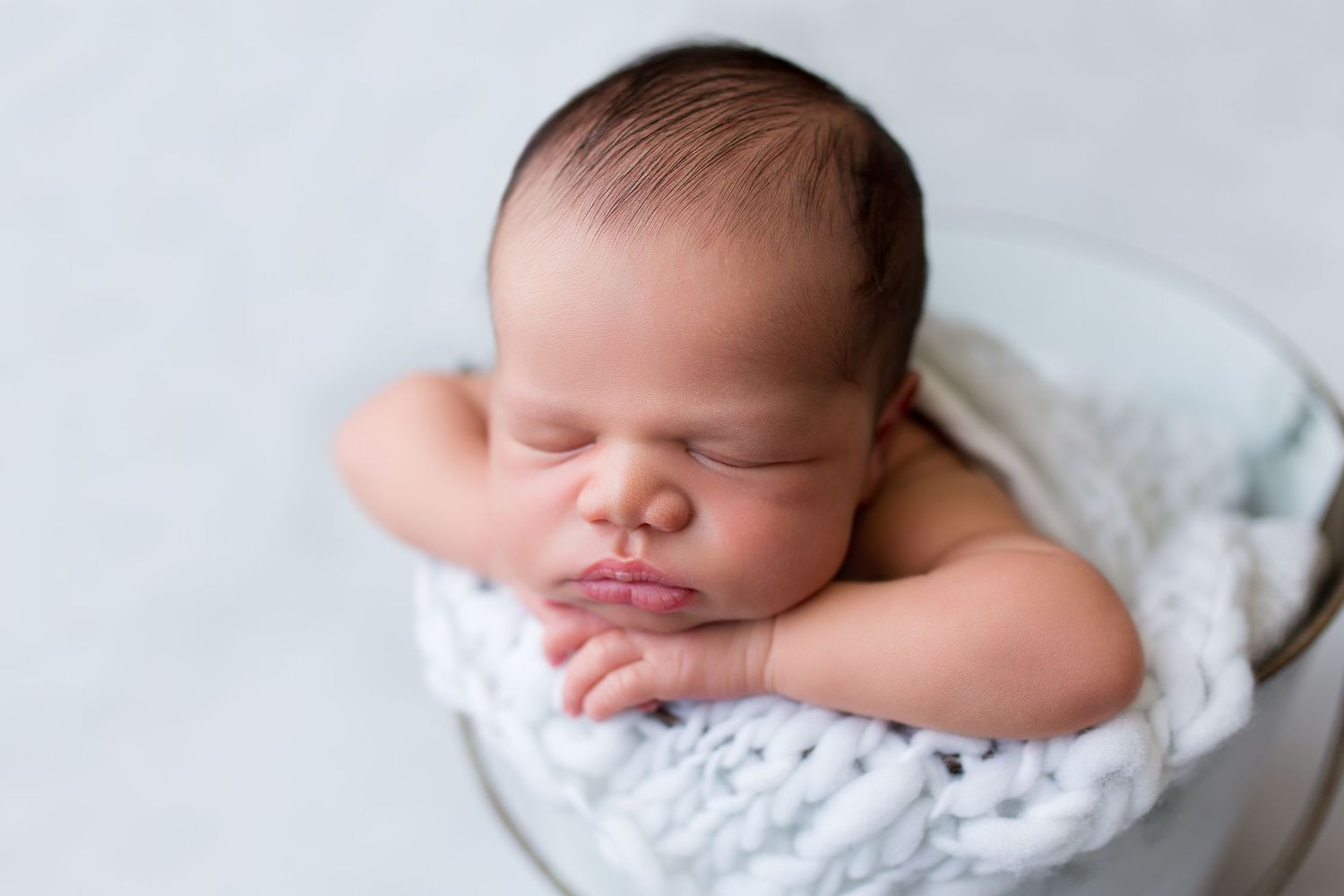 Sleeping newborn on soft white blanket with natural lighting.