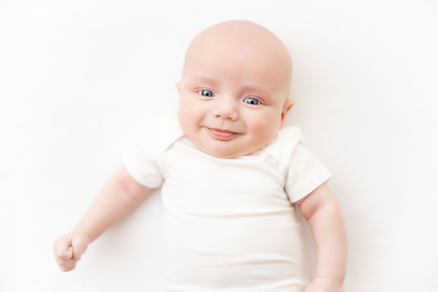 Baby in white onesie lying on white background during minimalist photography session.