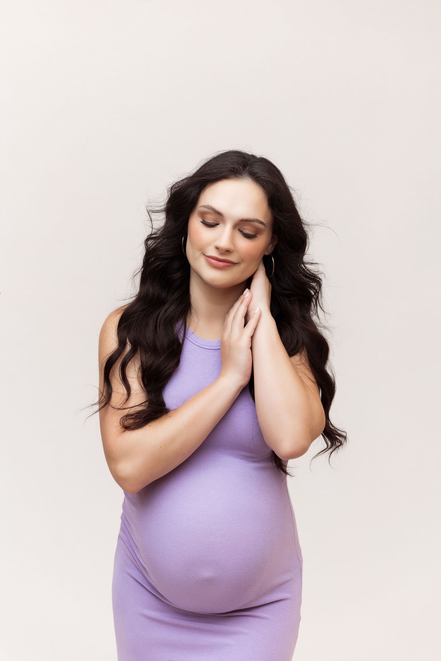 Side view maternity portrait with woman in purple dress against white background.