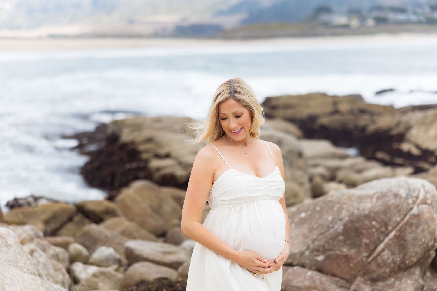 Coastal maternity photography session on rocky beach with ocean waves.
