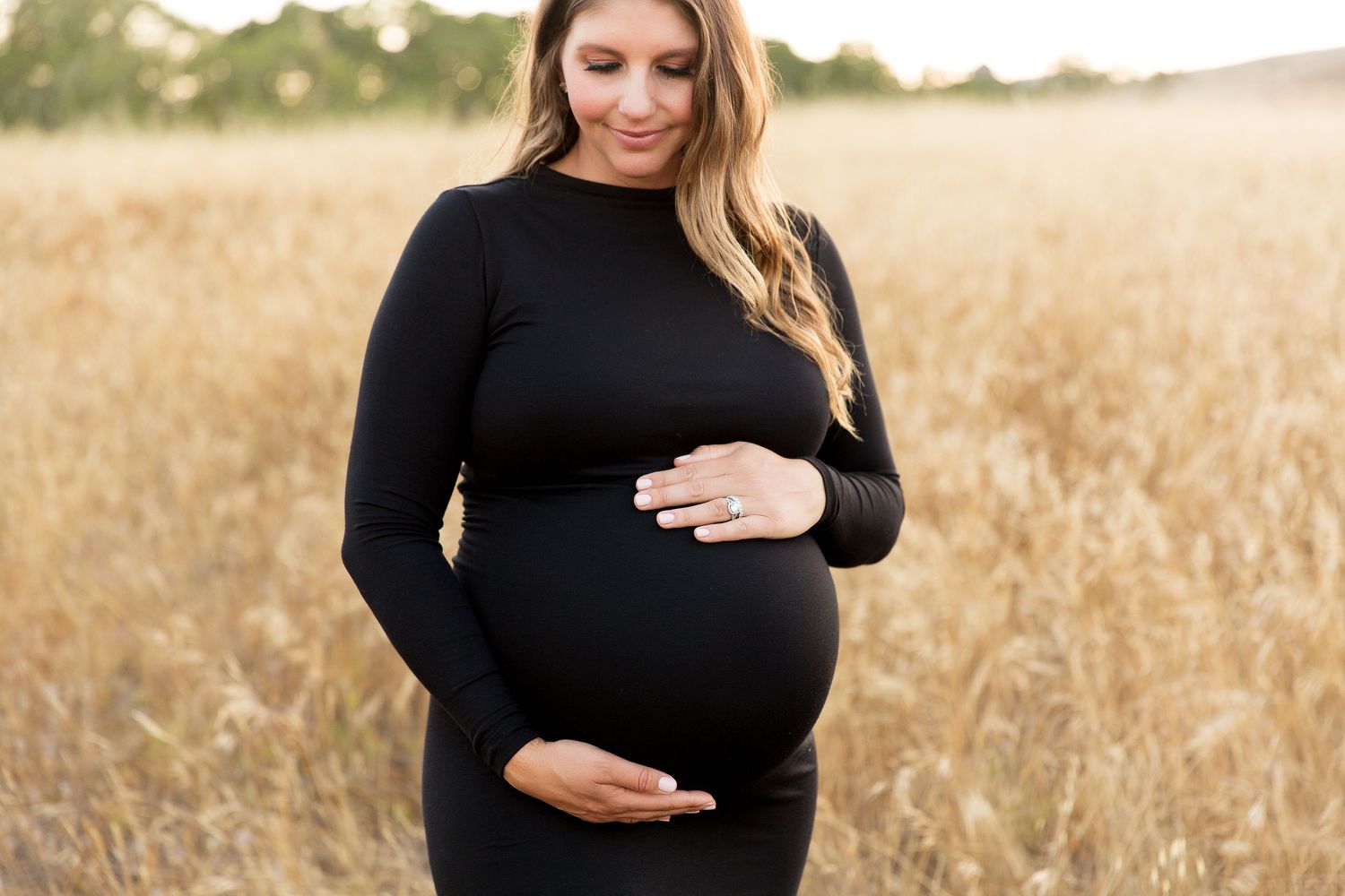 Maternity photo session in a sunlit field with golden grass.
