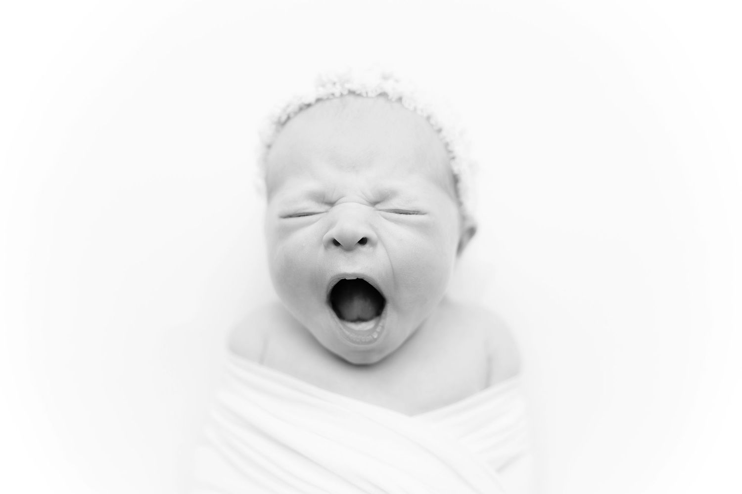 Black and white portrait of crying newborn baby wrapped in white fabric.