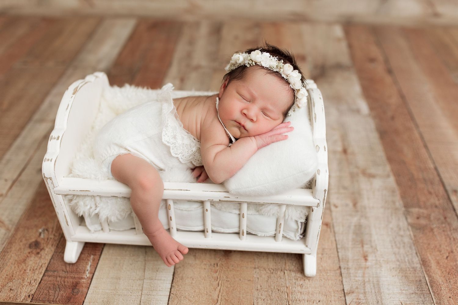 Peaceful newborn baby sleeping on vintage white bed prop during portrait session.