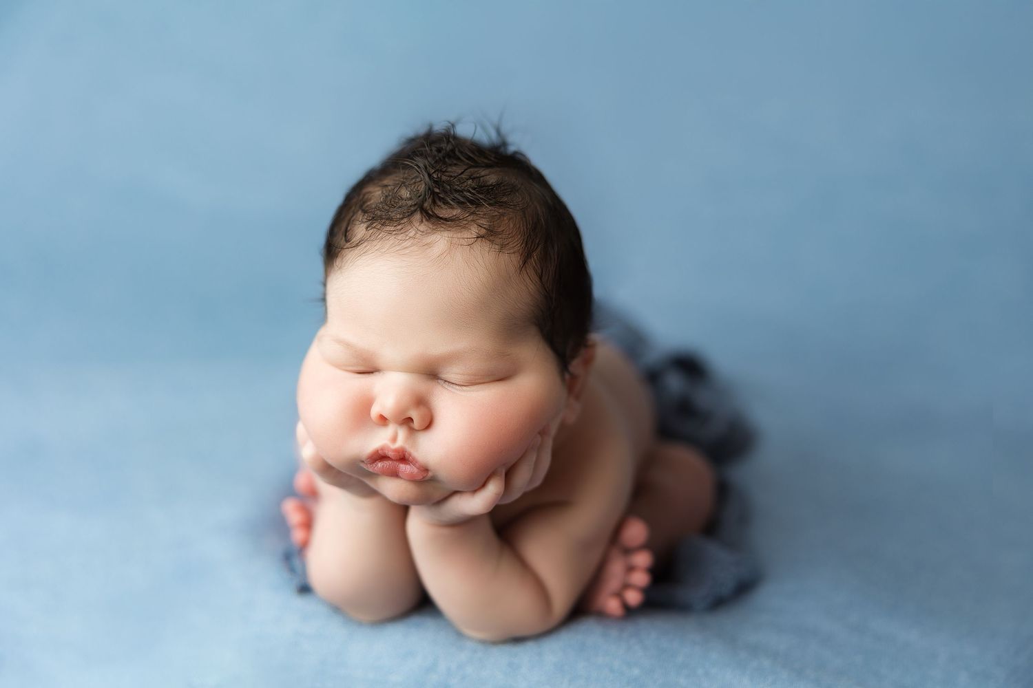 Newborn baby resting on blue backdrop during professional photography session.