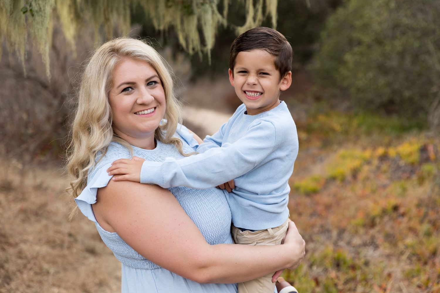 Parent and child in matching light blue outfits embrace while posing outdoors.