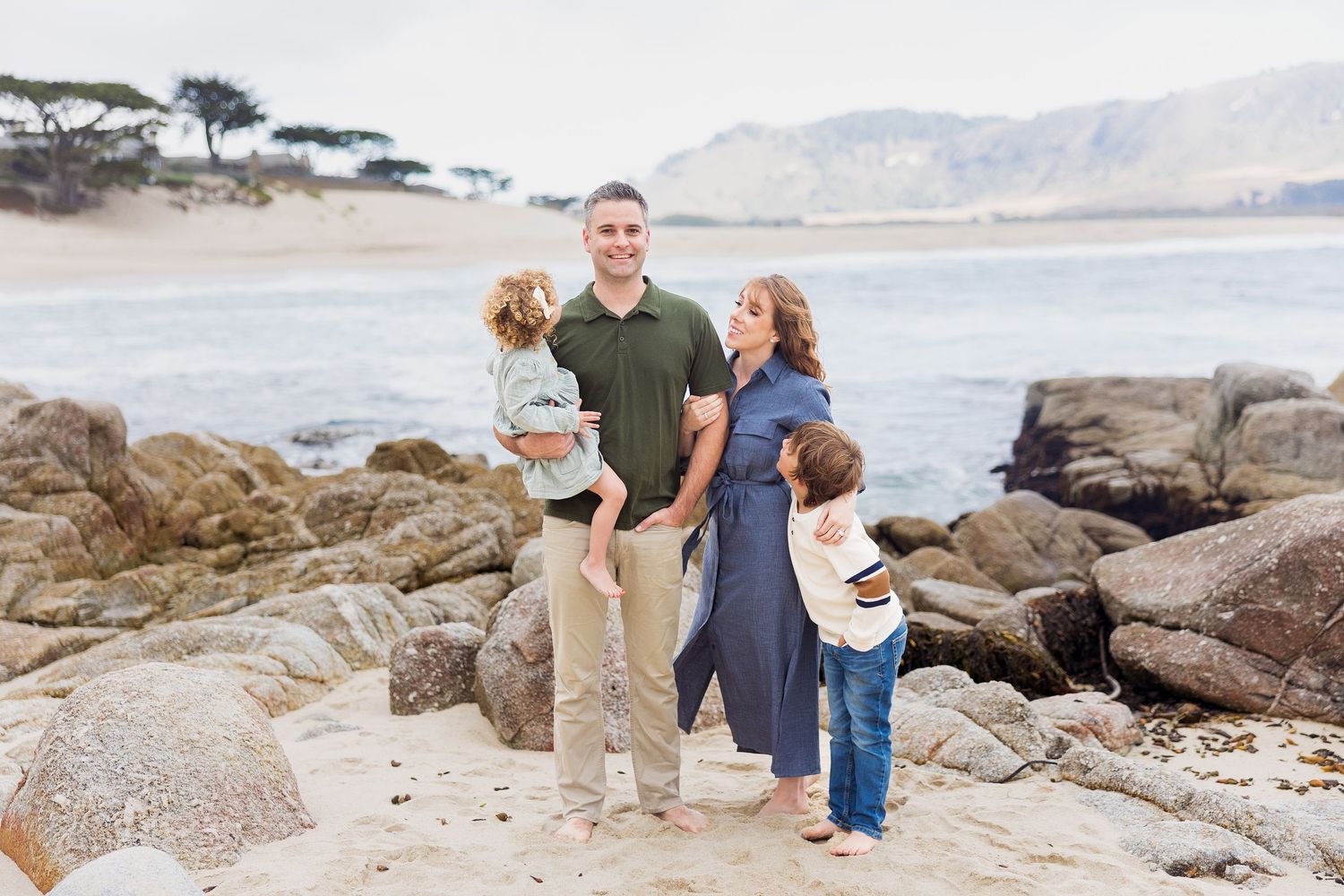 Family poses together on rocky coastline with ocean and mountains in background.