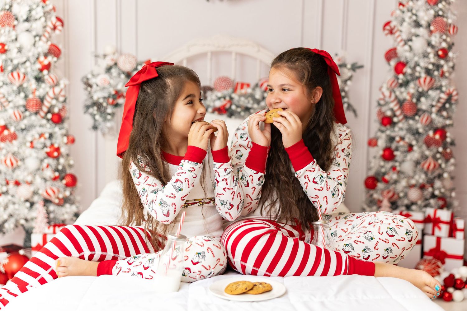 Children enjoying Christmas cookies on white bedding with festive holiday decorations.