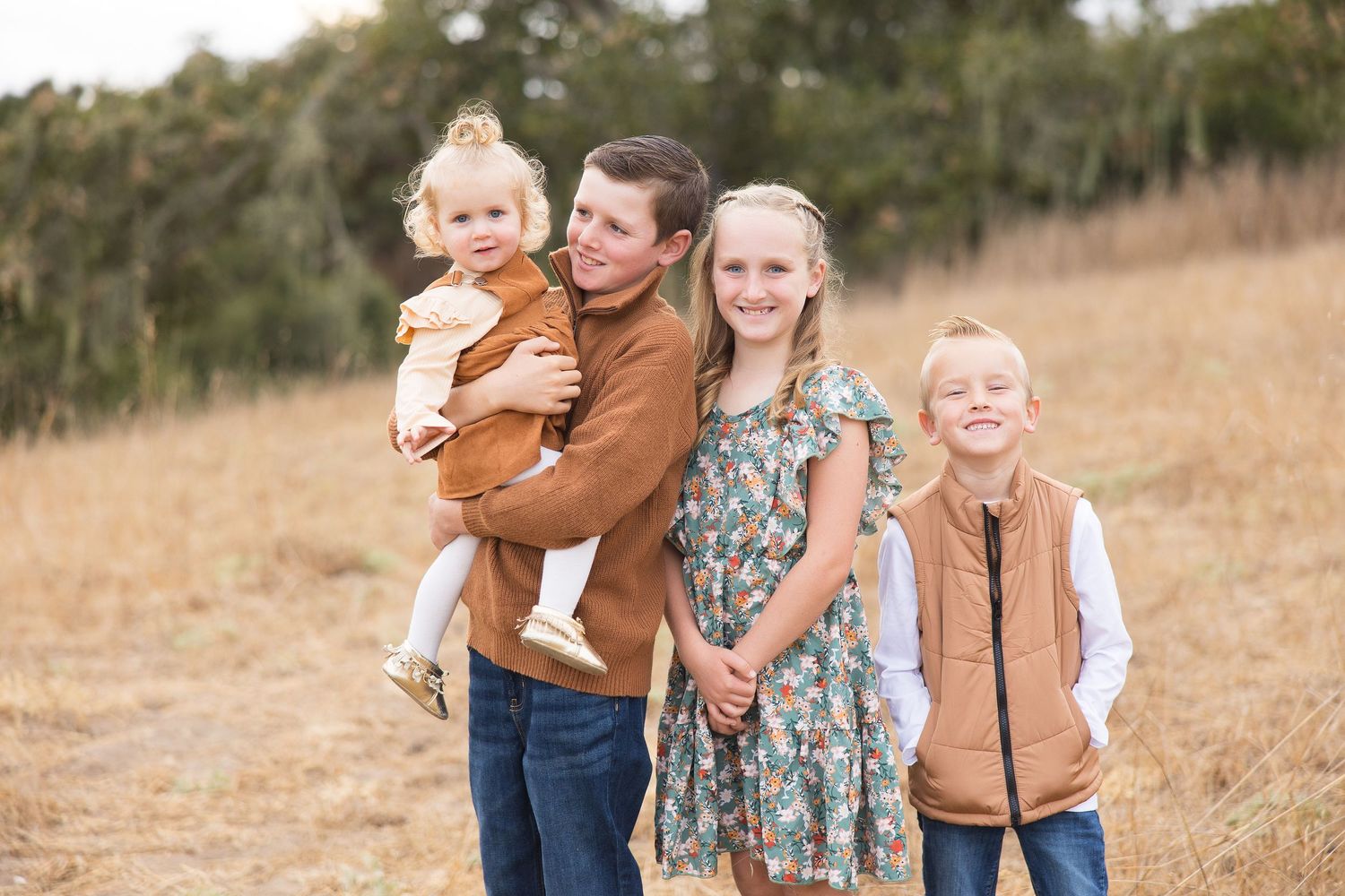 A family wearing fall colors poses together in a golden grassy field during an autumn outdoor photoshoot.