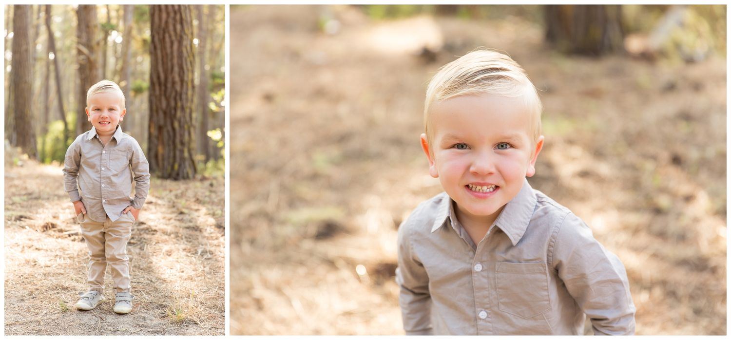 A young child wearing casual clothing poses outdoors in a natural setting with trees and dry grass in the background.