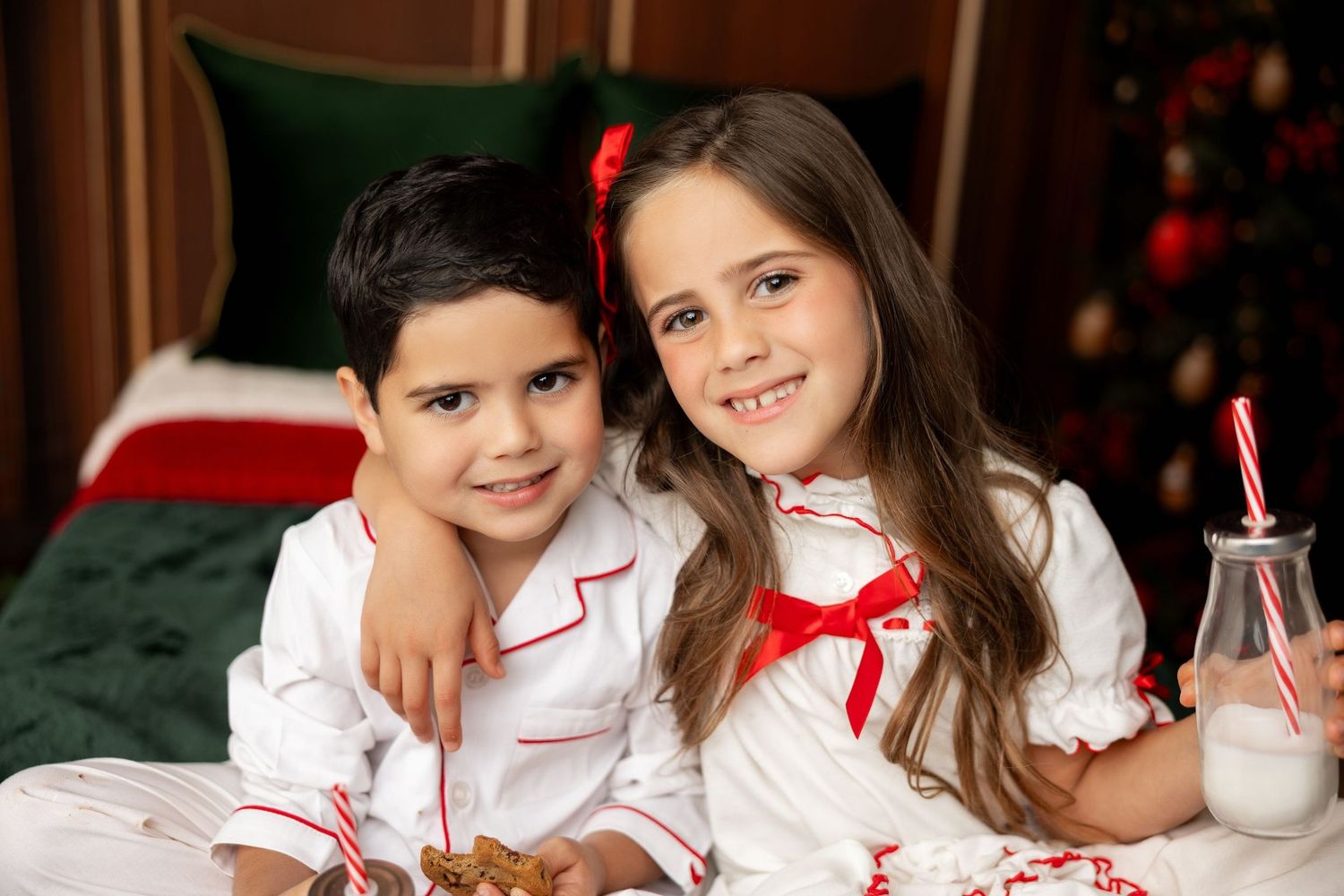 Siblings in Christmas pajamas with milk and cookies on a holiday bed at a mini session in Pacific Grove