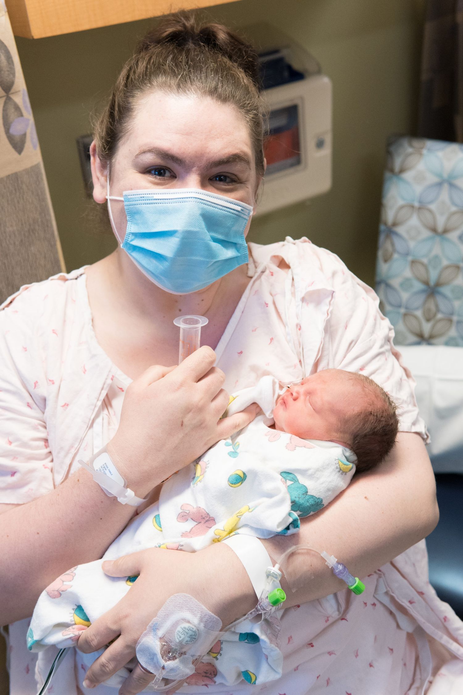 Healthcare worker in protective mask and gloves holding and feeding a newborn baby in a hospital setting.