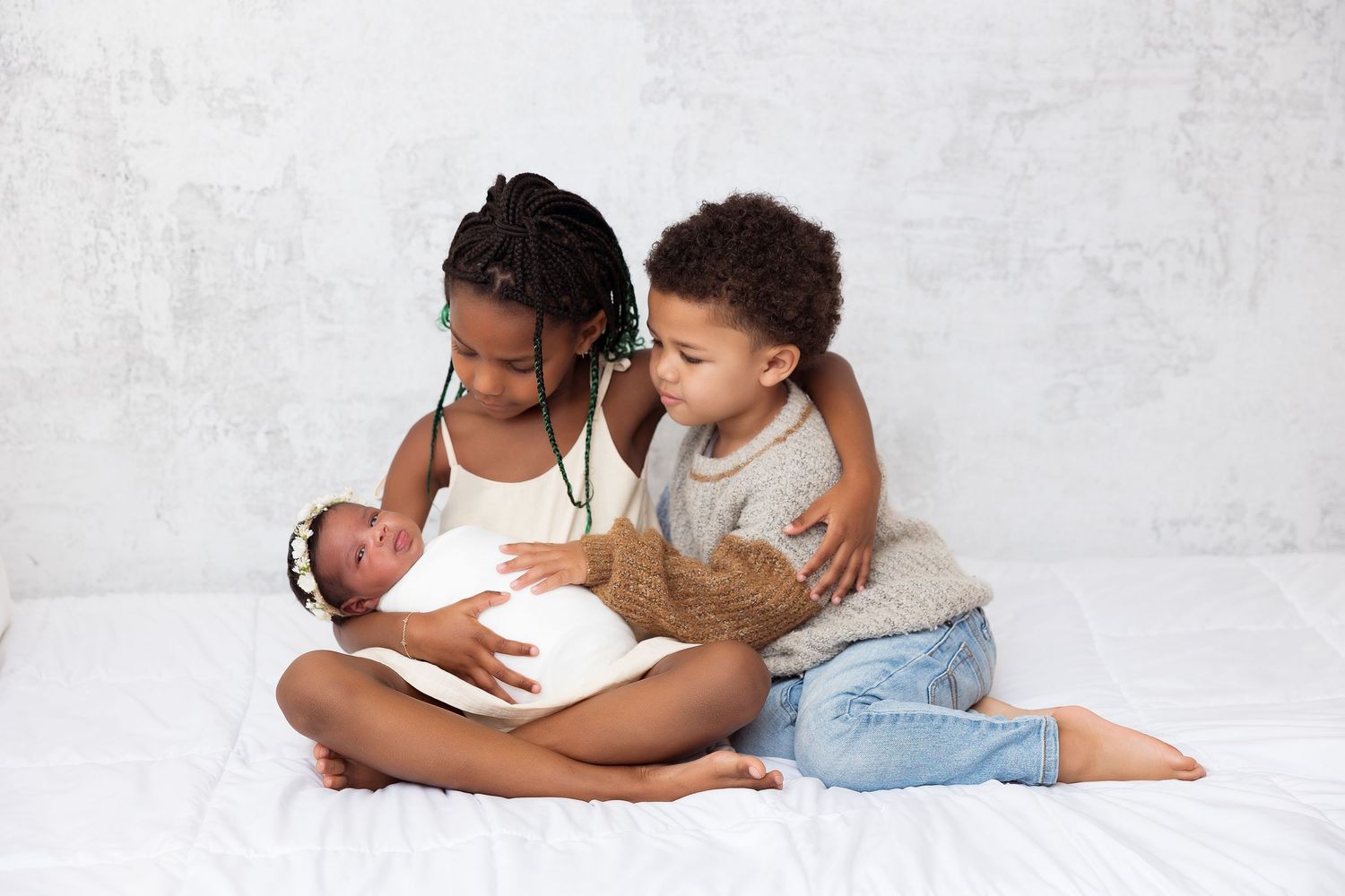 Children cuddling with newborn baby on white background.