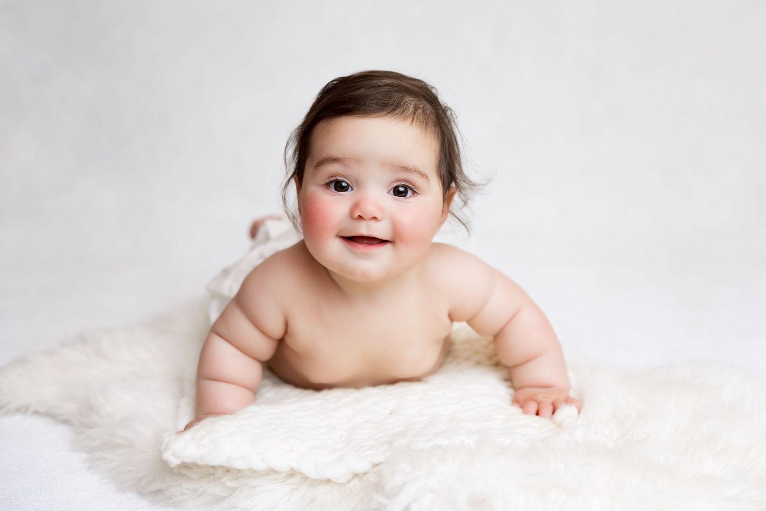Adorable baby lying on soft white fur blanket in minimalist portrait style.
