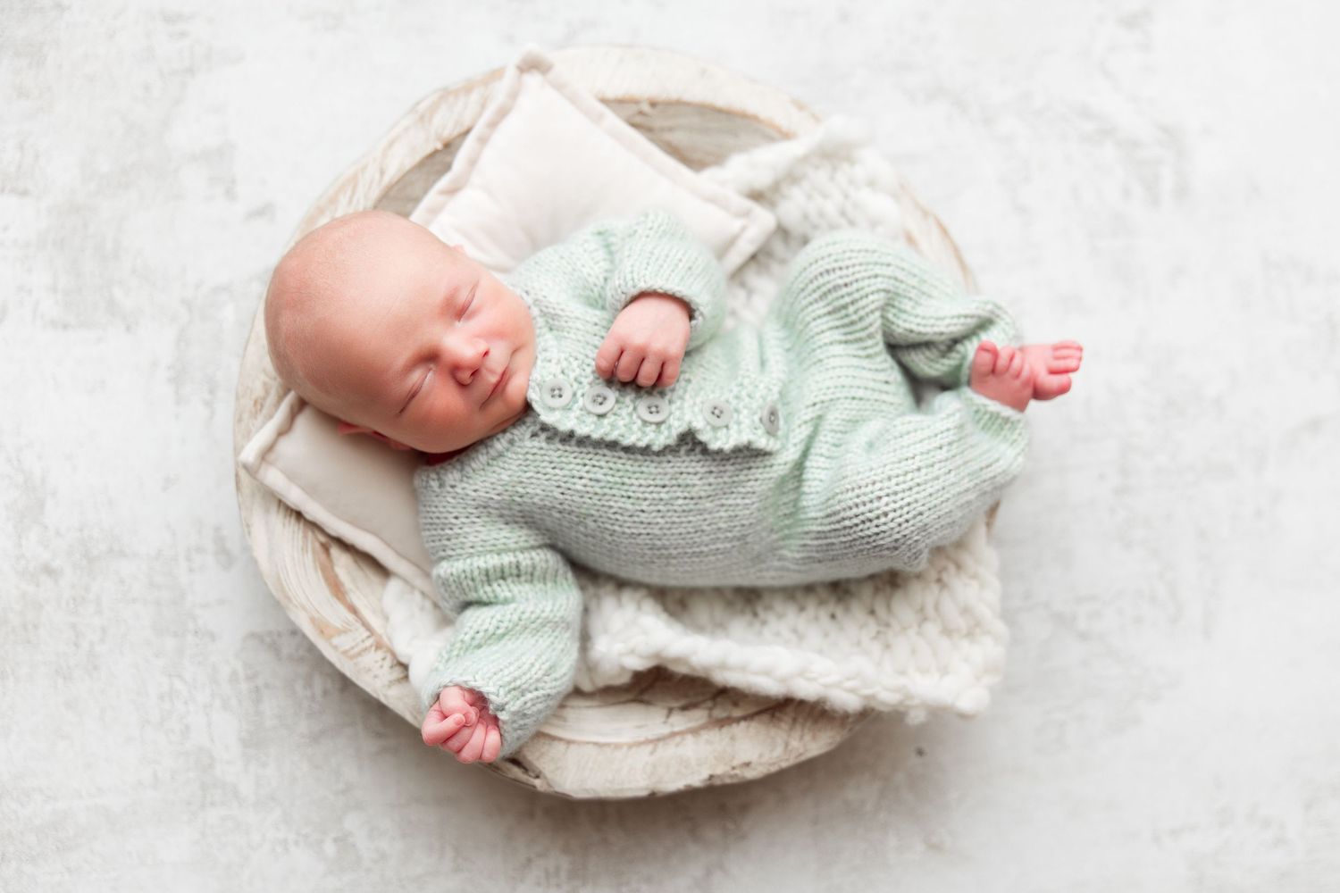 Newborn wearing mint green knit sweater on cream blanket.