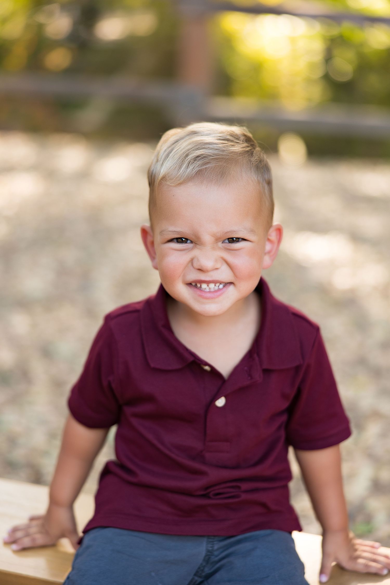 Young boy in burgundy polo shirt smiling during outdoor portrait session.