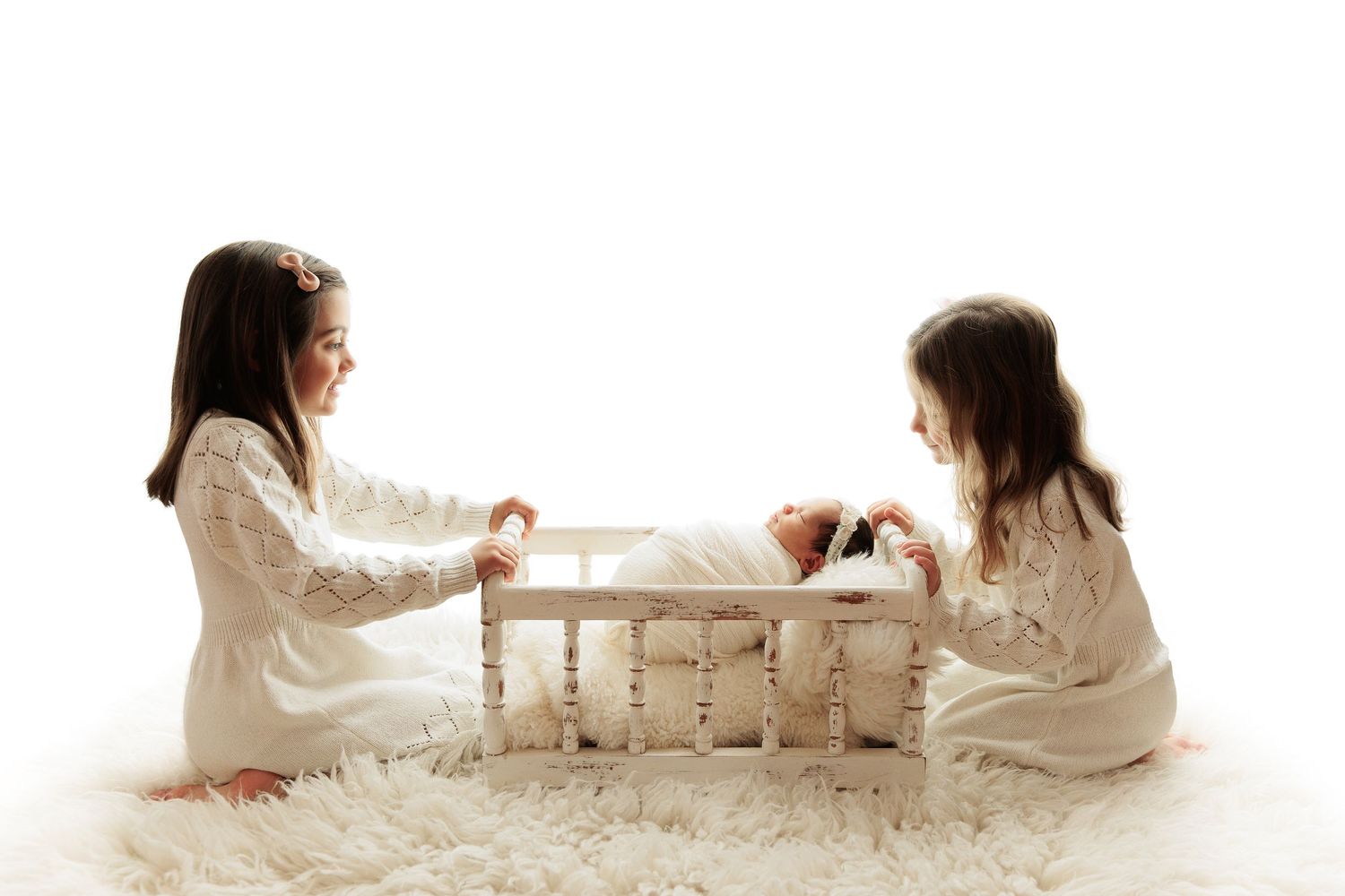 Two children in white dresses playing with letter blocks on fluffy rug.