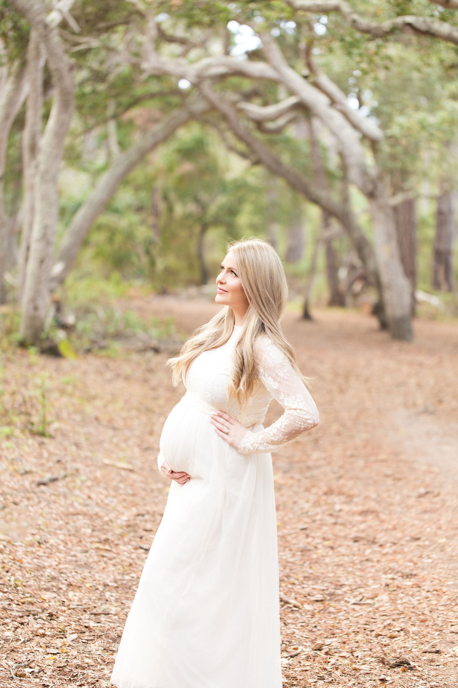 A woman in a flowing white dress twirls gracefully among autumn trees in a forest setting.