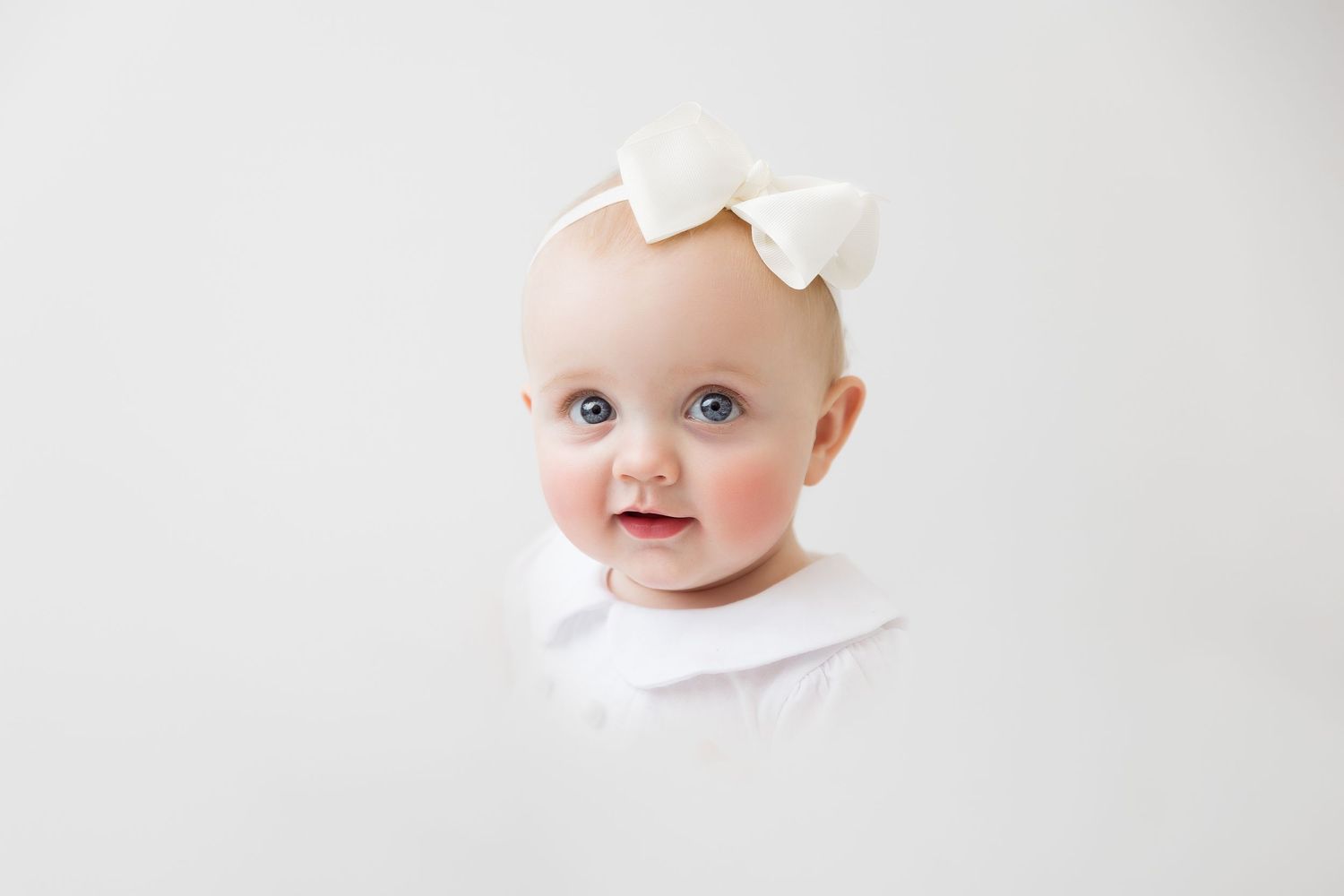 Simple white studio portrait of baby wearing delicate bow headband. heirloom portrait