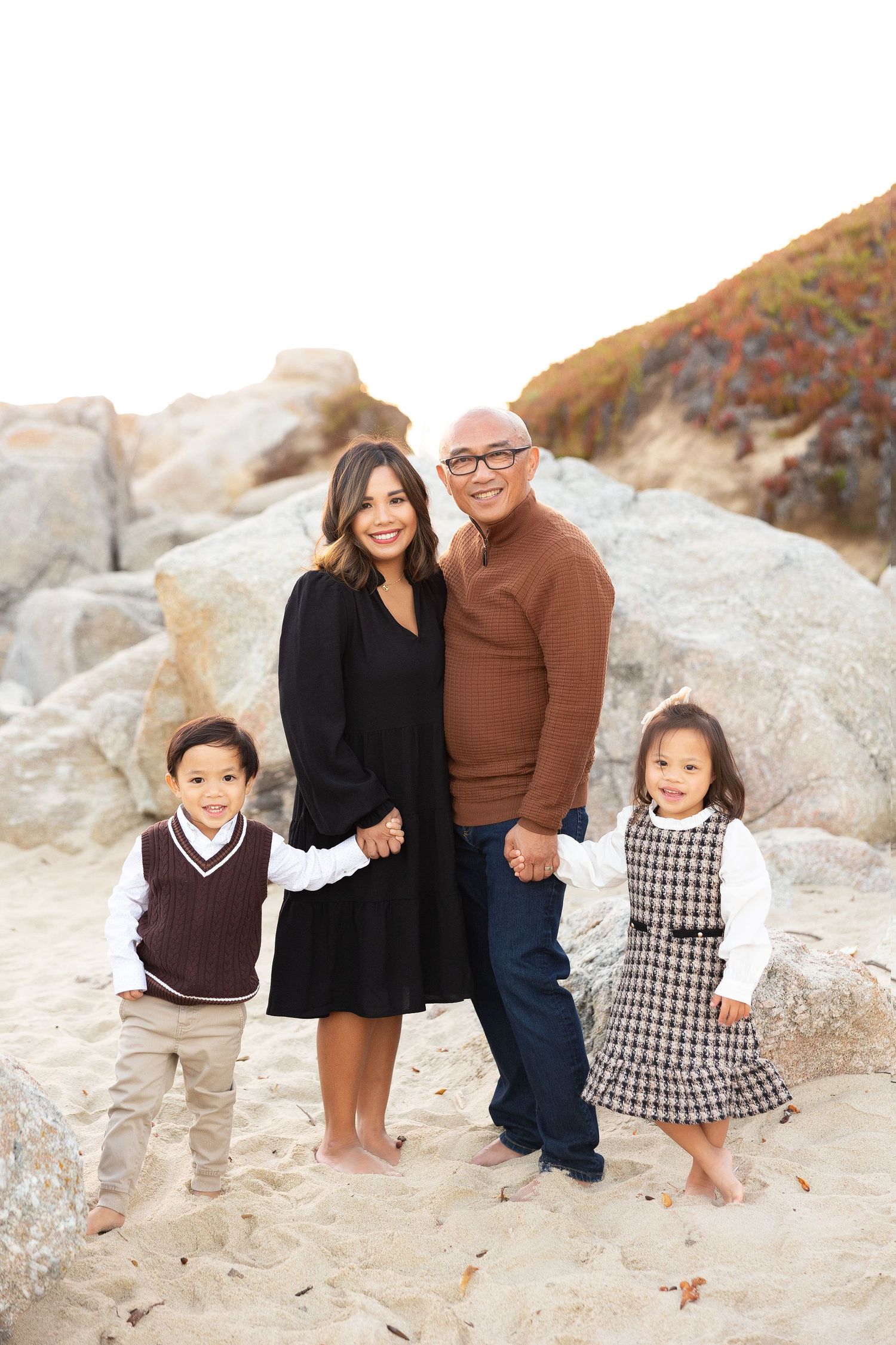 Family of four poses together on rocky beach during sunset photoshoot.