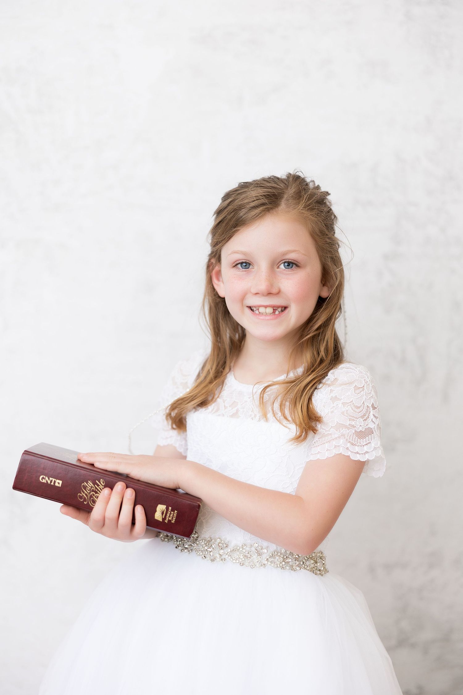 A portrait in white lace dress holding a religious book against a light background.