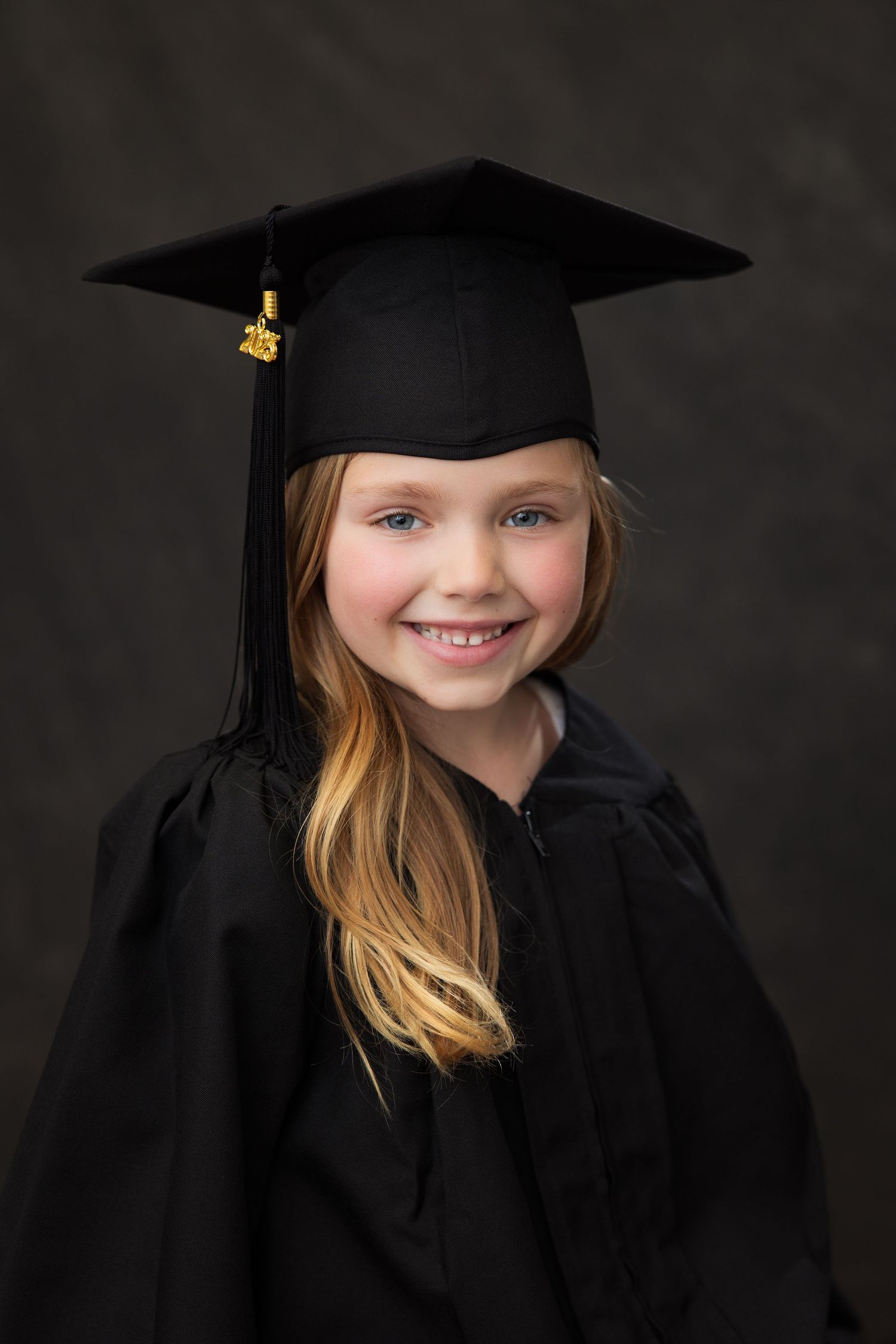 A graduate portrait featuring a traditional black cap and gown against a dark background.