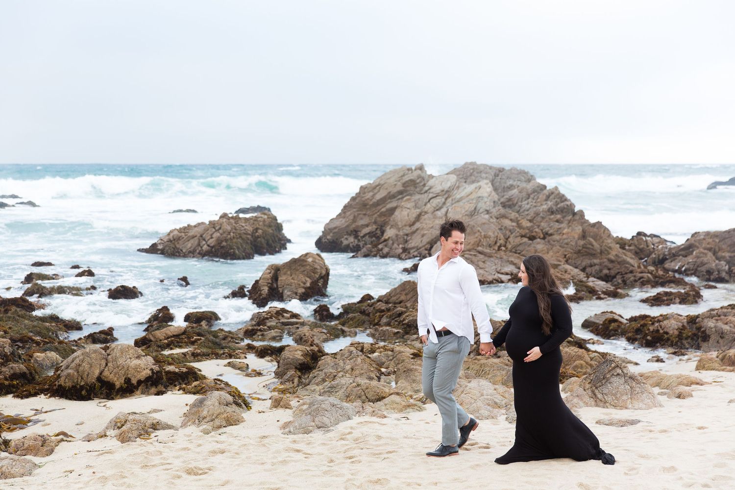 Couple posing together on a rocky beach with waves crashing in the background.