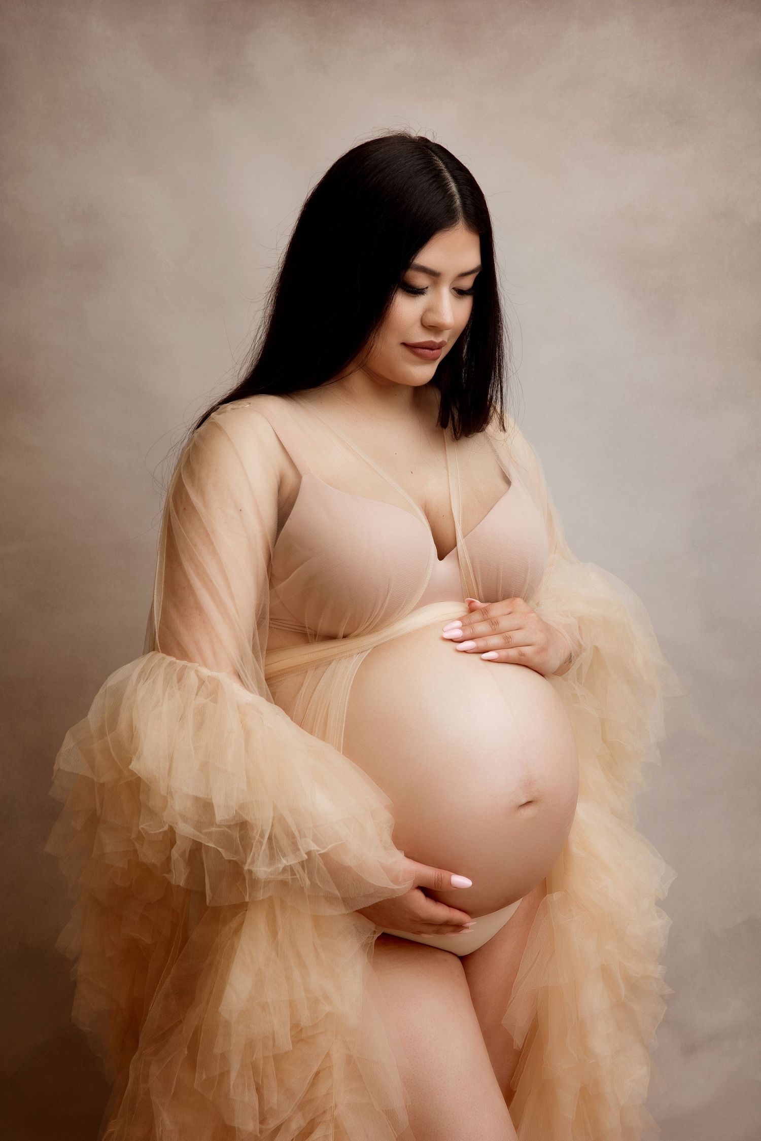 Intimate maternity portrait in peachy tulle dress against neutral background.
