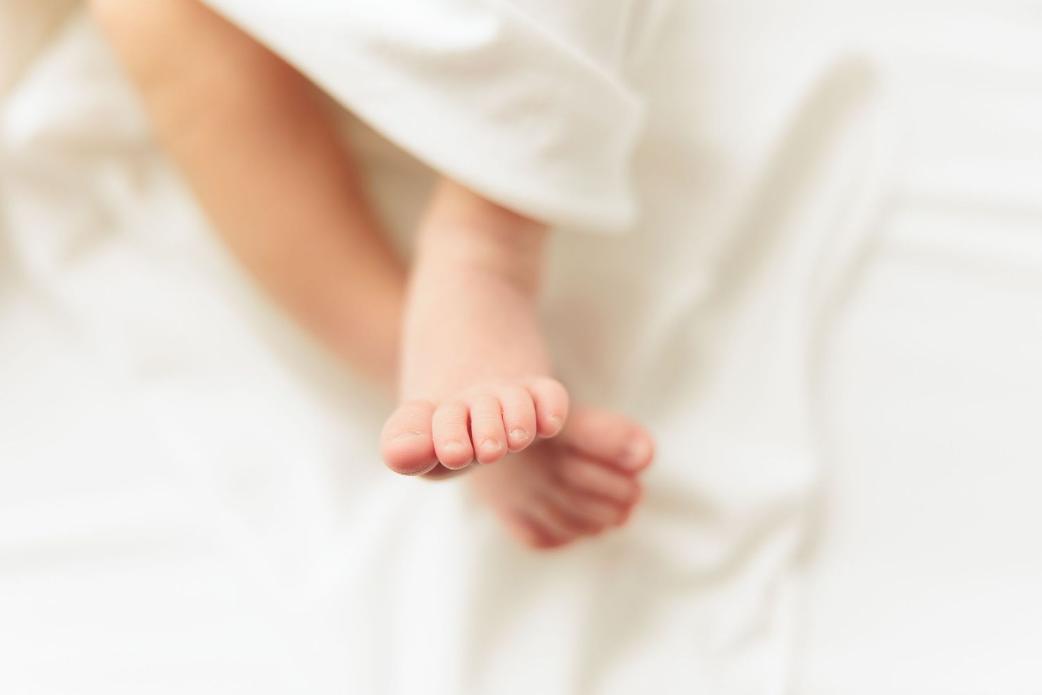 Tiny newborn baby feet resting on soft white fabric in natural light.