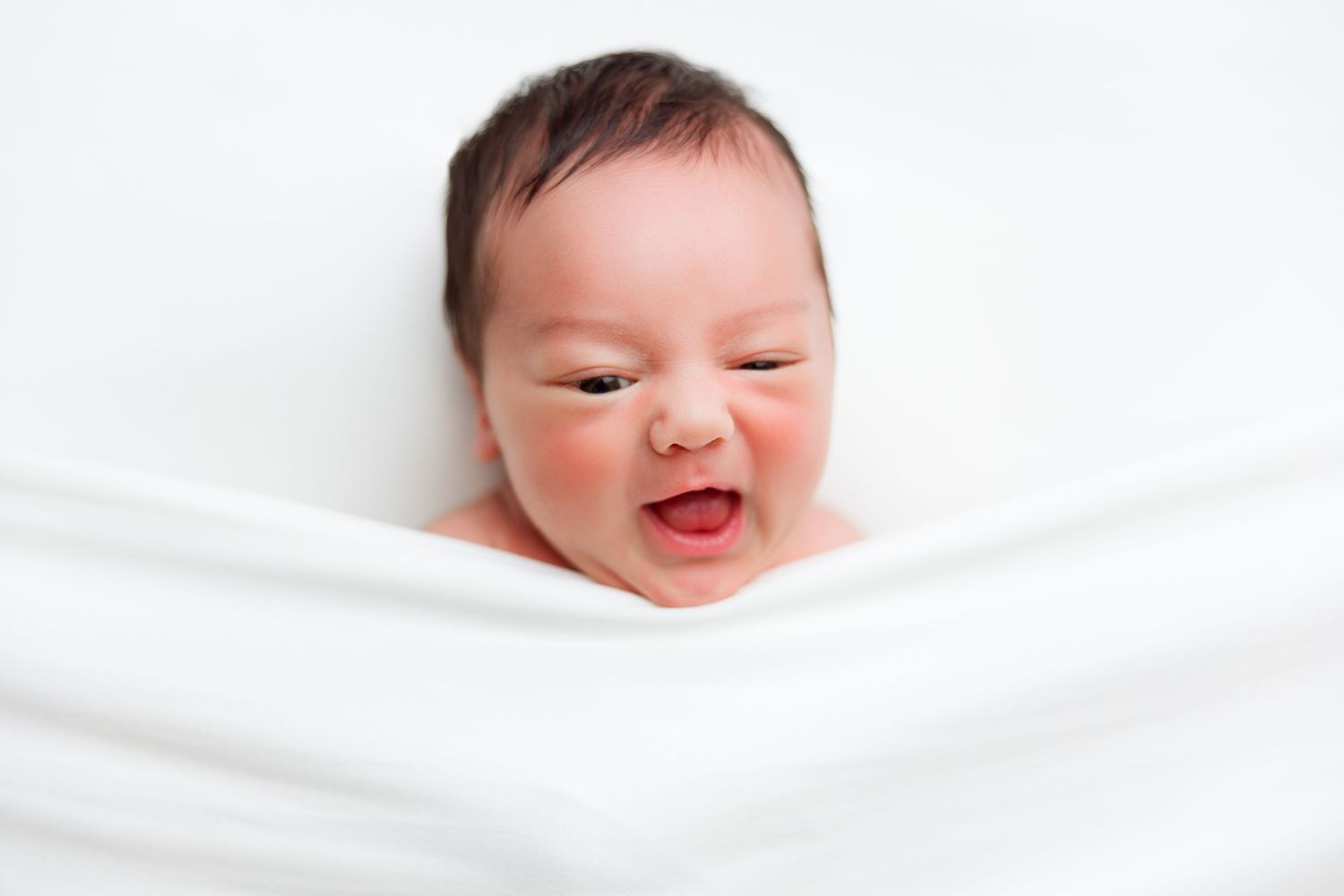 Happy baby smiling while wrapped in white blanket.