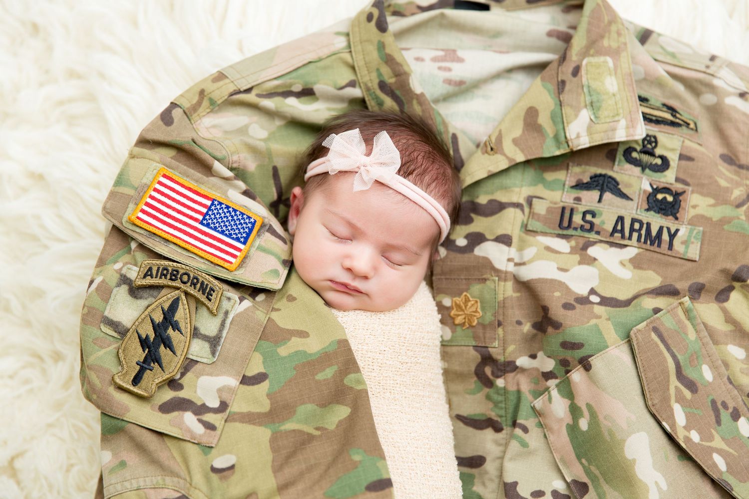 A newborn baby sleeps peacefully while wearing U.S. Army military camouflage uniform and American flag patch.