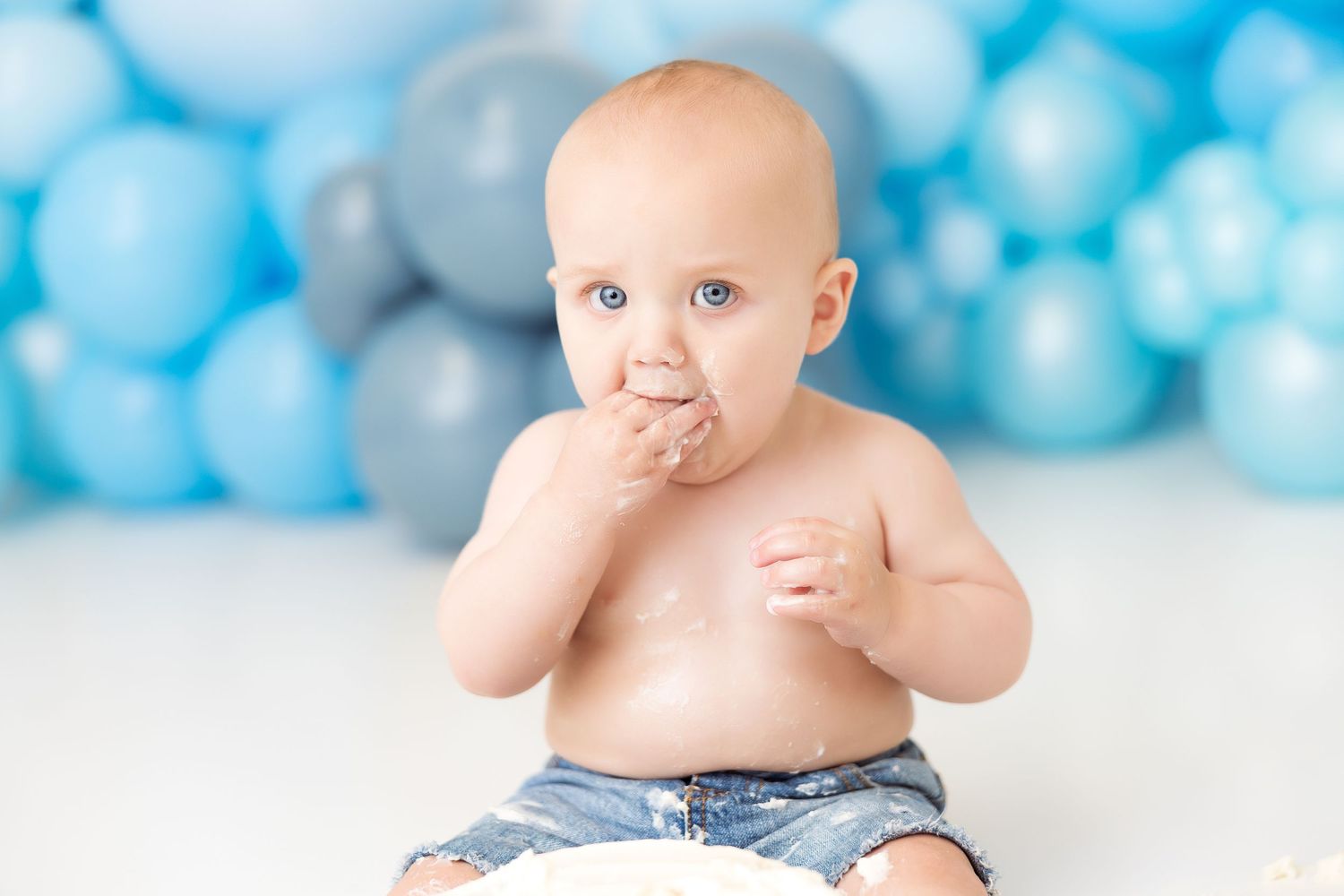 A baby in blue denim on a white floor with blue bokeh lights in the background.