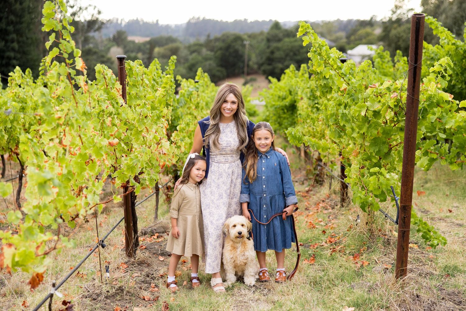 Mom and two daughters with their dog among green grapevines during a Santa Cruz family photo session.