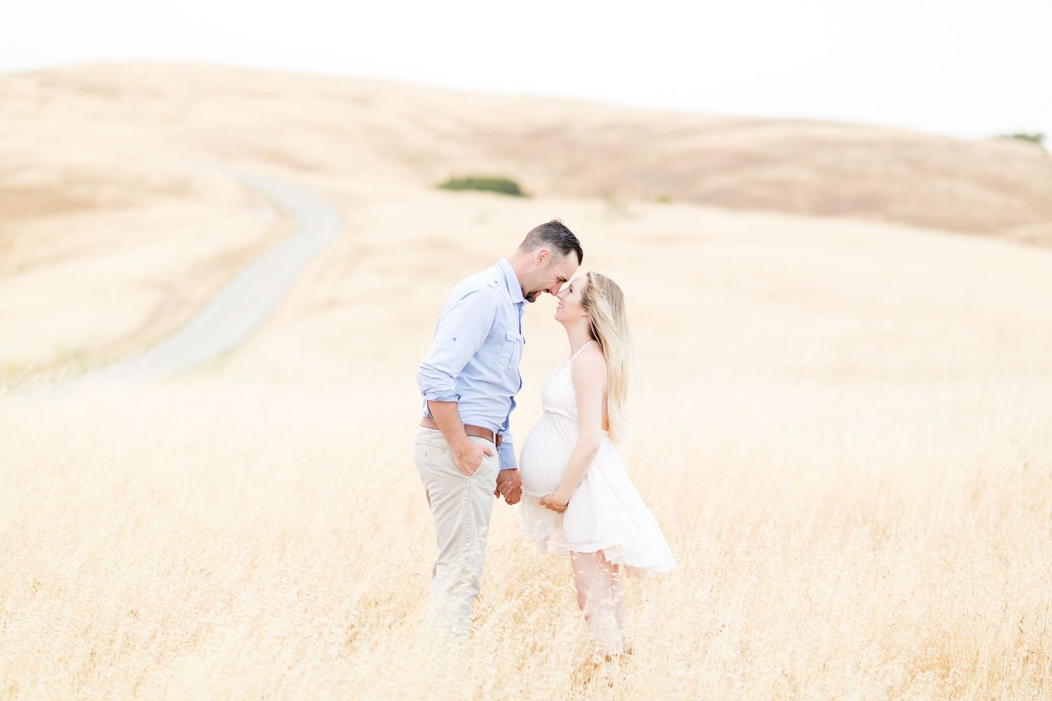 A romantic couple shares tender moments in a sun-drenched field of tall grass.