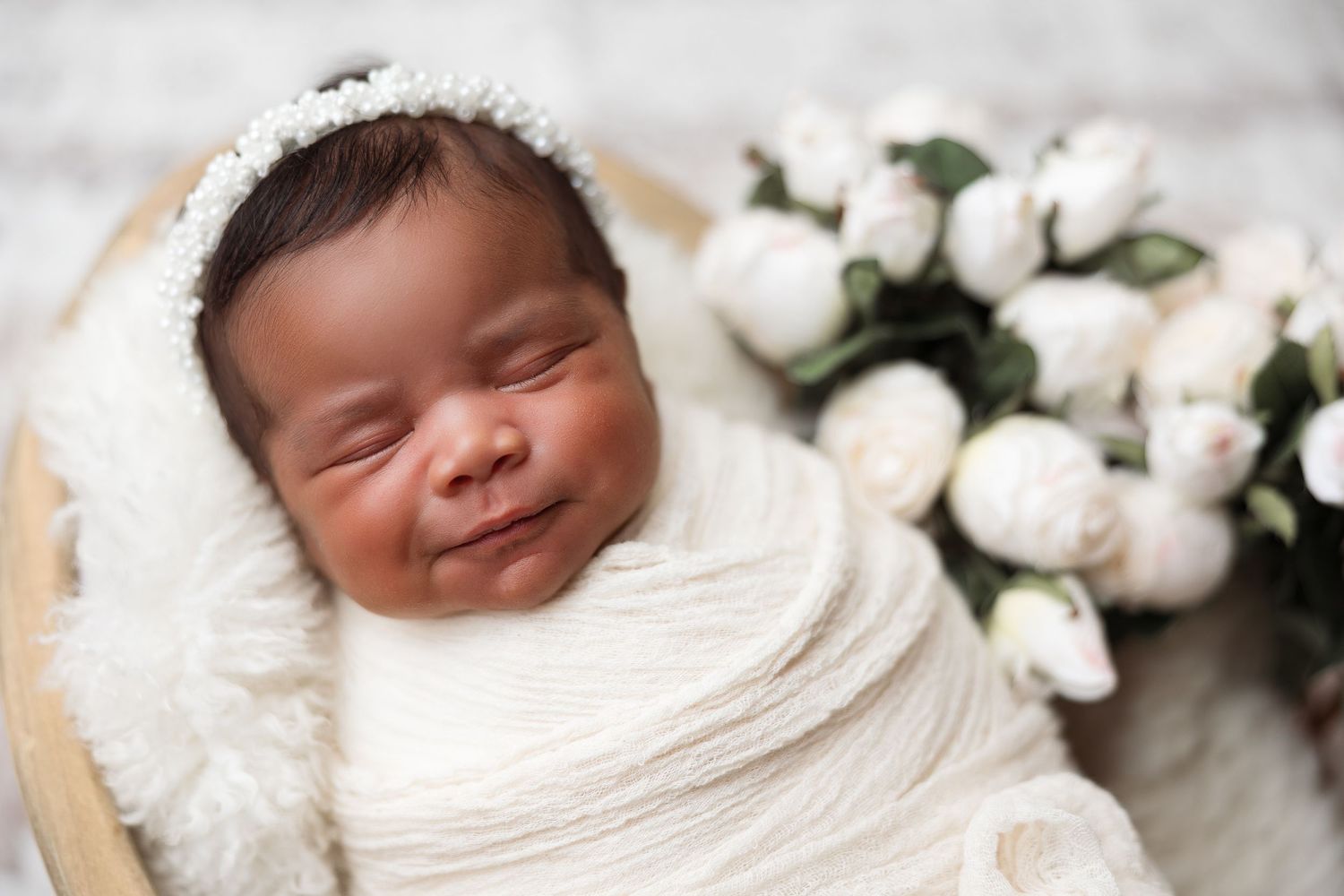 Smiling newborn wrapped in white blanket with white roses.
